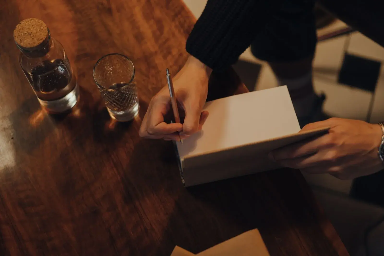 Une personne écrit une dédicace sur la page d’un livre posé sur une table en bois.