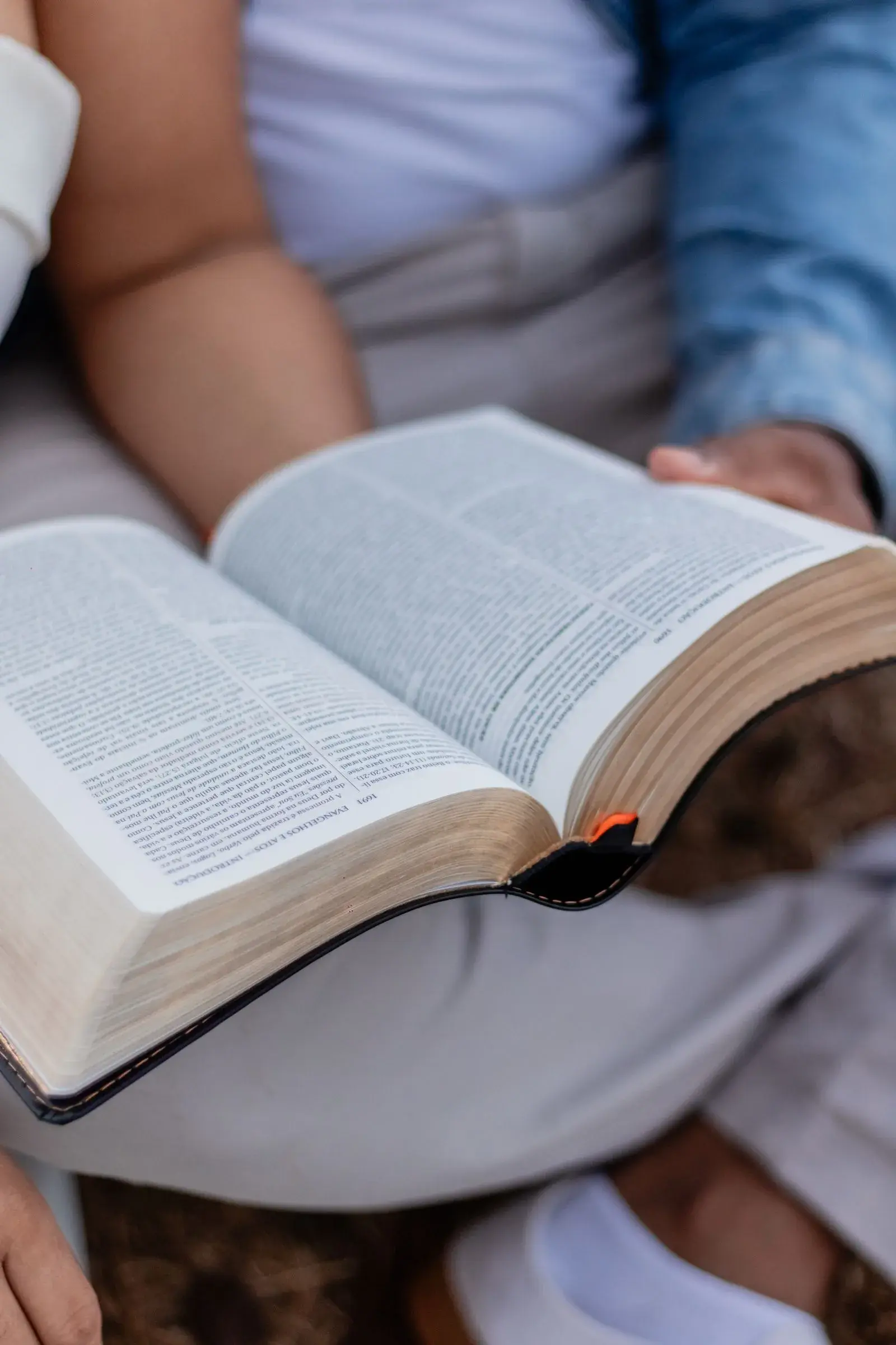 Deux personnes partagent la lecture d’un livre ouvert posé sur leurs genoux.