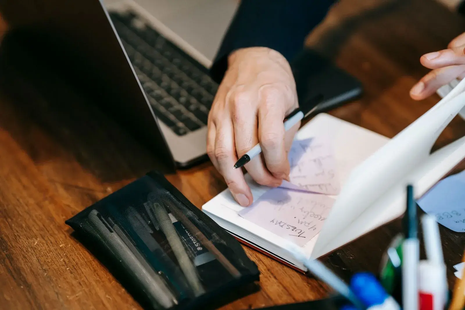 Des mains prennent des notes dans un carnet, à côté d’un ordinateur portable.